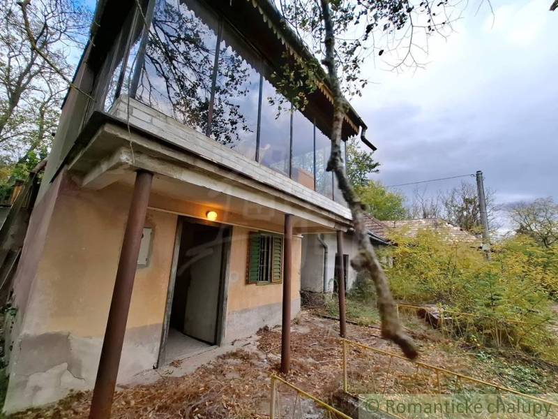 Chata v Kamenínu se zaskleným balkonem, okolní příroda a zarostlý dvůr.