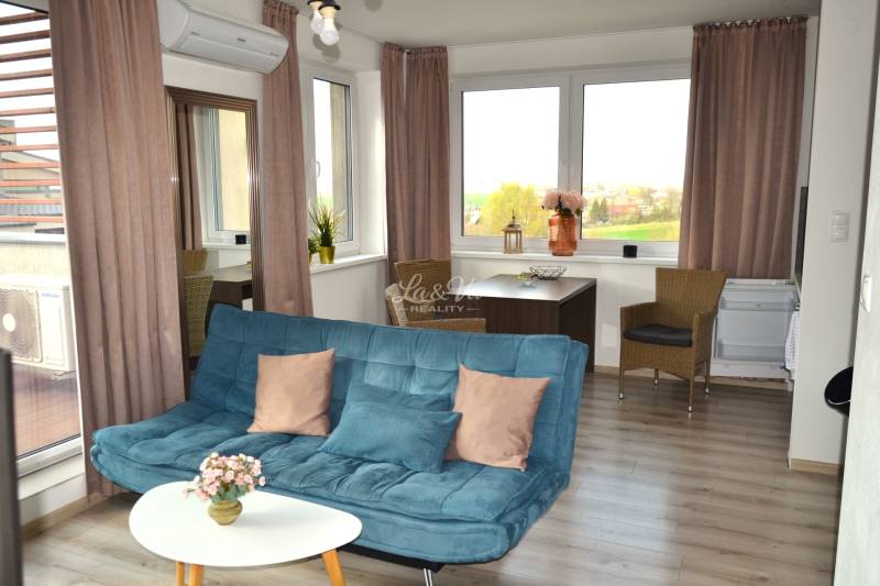 Obývací pokoj s pohovkou, stolkem, rostlinami a podlahou s dřevěným dekorem v 2pokojovém bytě.