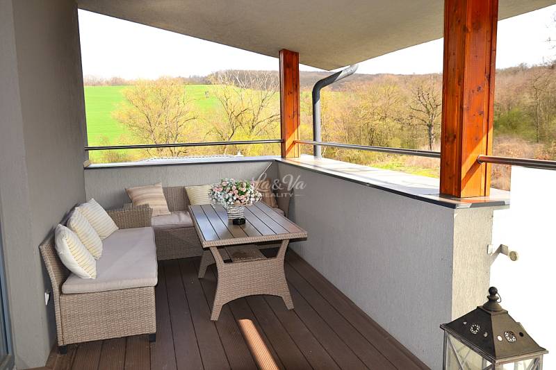 Prostorný balkon s ratanovým nábytkem a podlahou s dřevěným dekorem v garsonce.