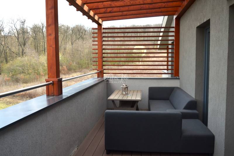 Balkon 2-pokojového bytu s dřevěným dekorem a výhledem na zeleň.