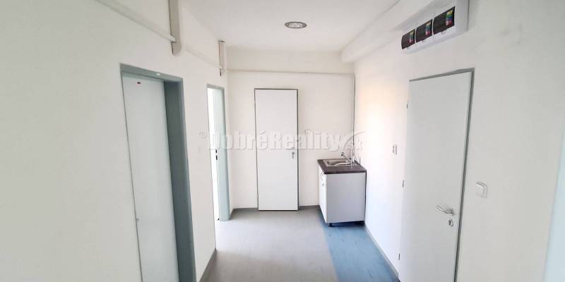 Kanceláře s umyvadlem a dveřmi, podlaha s dřevěným dekorem, bílé stěny.