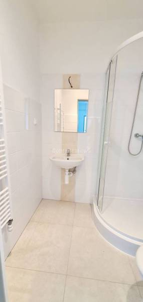 Koupelna s umyvadlem, sprchovým koutem a bílými obklady v kanceláři.