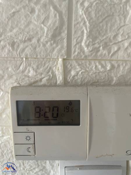 Termostat na bílé stěně v třípokojovém bytě ukazuje 19,6 °C.