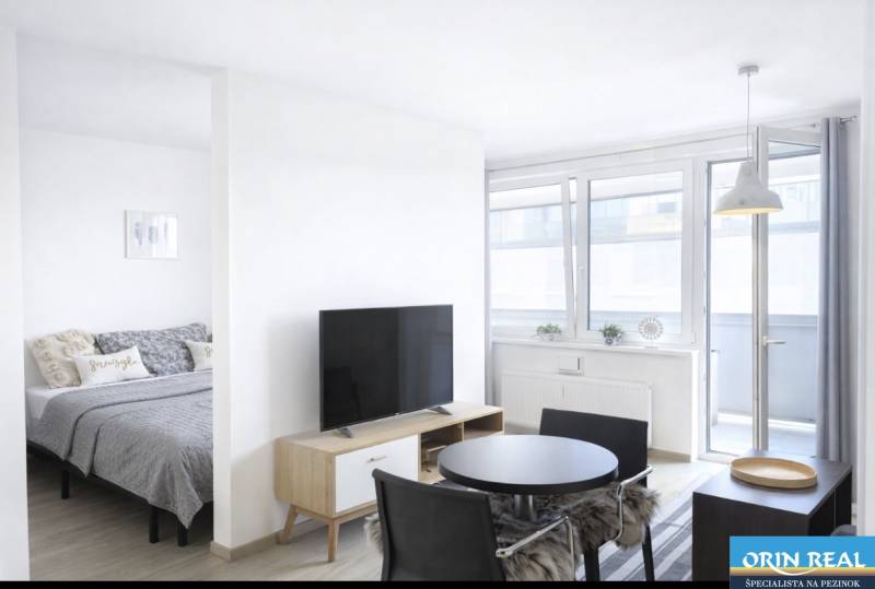 Světlý obývací pokoj v 2-pokojovém bytě s televizí a jídelním stolem.