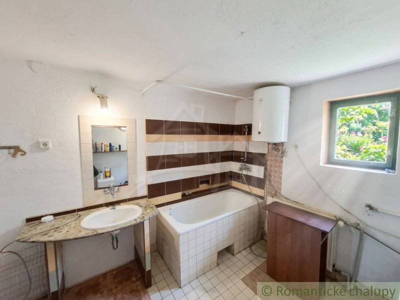 Koupelna v rodinném domě s umyvadlem, vanou a bojlerem.