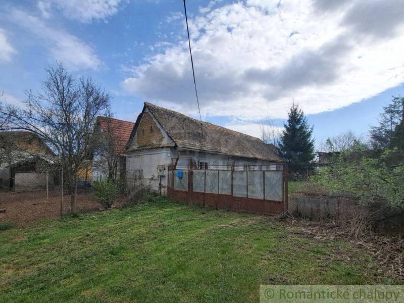 Rodinný dům v Ozdíně, obklopený zahradou a stromy, pod modrou oblohou.