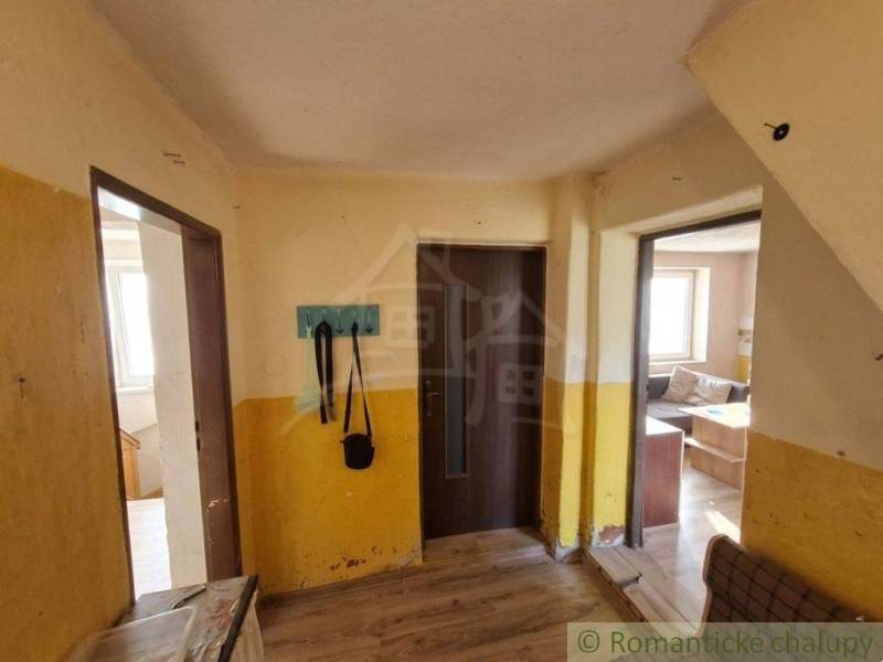 Interiér rodinného domu s podlahou s dřevěným dekorem, žluté stěny, věšák, pohovka.