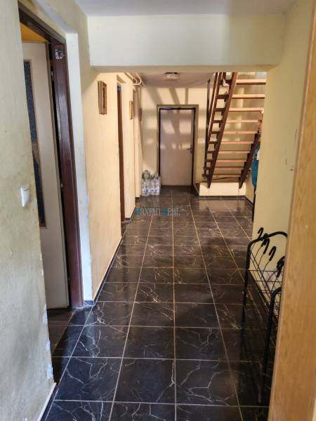 Interiér rodinného domu s tmavou dlažbou a dřevěným schodištěm.