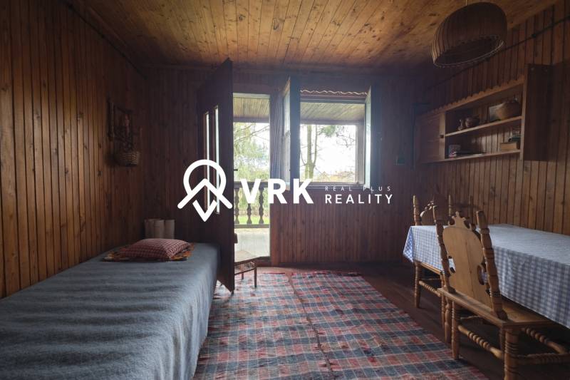 Interiér chaty s dřevěným dekorem, postel, stůl, židle a kobereček.