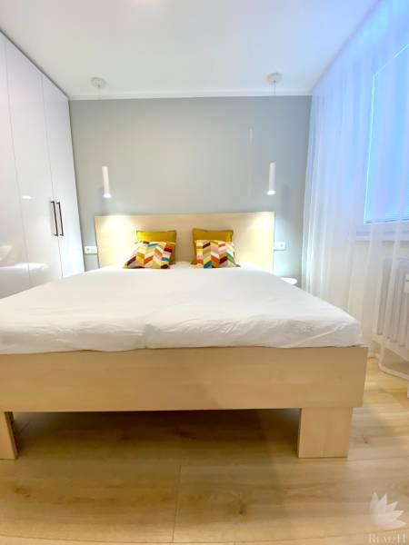 Světlá ložnice v dvoupokojovém bytě s barevnými polštáři na posteli.