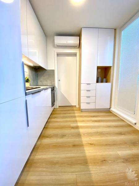 Kuchyně s bílými skříňkami a podlahou s dřevěným dekorem v 2-pokojovém bytě.