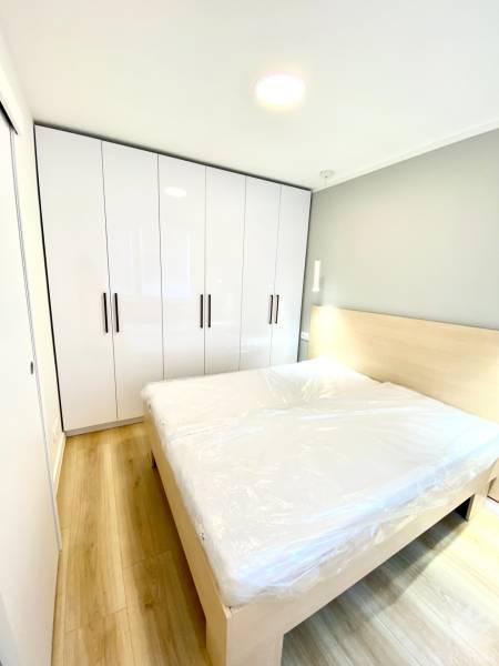 Ložnice s manželskou postelí, bílou skříní a podlahou s dřevěným dekorem ve dvoupokojovém bytě.