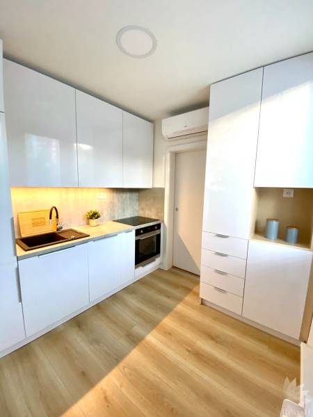 Kuchyně v 2-pokojovém bytě s bílými skříňkami a podlahou s dřevěným dekorem.