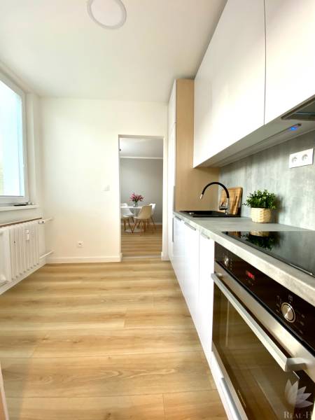 Kuchyně v 2pokojovém bytě s bílými skříňkami a podlahou s dřevěným dekorem.