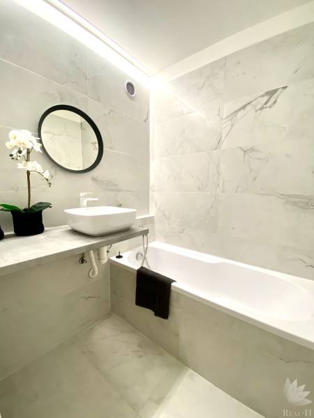 Koupelna v 2-pokojovém bytě s vanou, zrcadlem a květinovou dekorací.