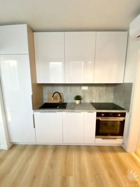 Kuchyňská linka s bílými skříněmi, šedou pracovní deskou a podlahou s dřevěným dekorem, 2-pokojový byt.
