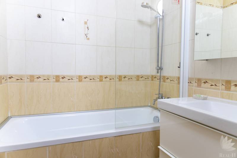 Koupelna s obkladem a vanou ve 4-pokojovém bytě, světlé barvy a sprchová růžice.