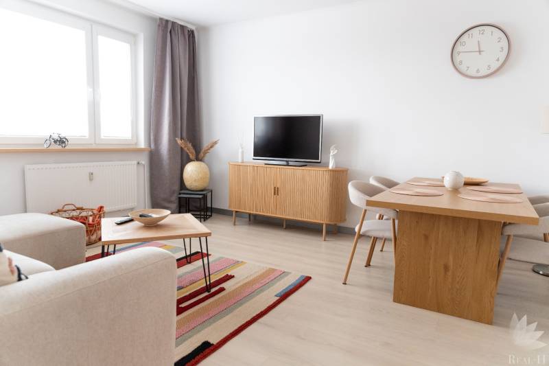 Obývací část 4pokojového bytu s TV, sedačkou, stolem a podlahou s dřevěným dekorem.