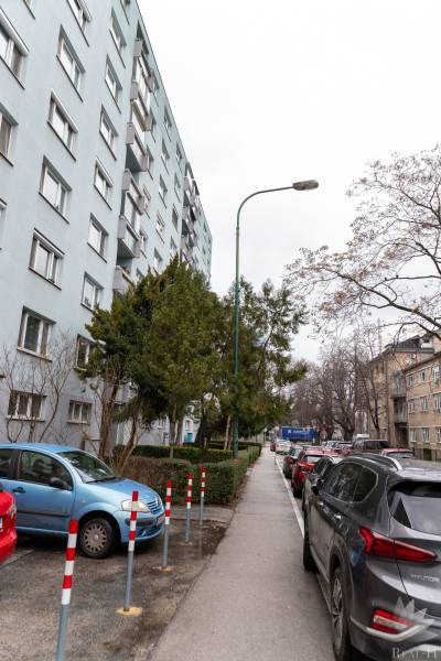 Vícepodlažní bytový dům na Ondavské ulici v Bratislavě - Nivy, obklopený auty a stromy.