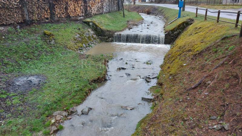 Potok protékající přes Rekreační pozemky v Púchově s dřevem uskladněným na okraji.