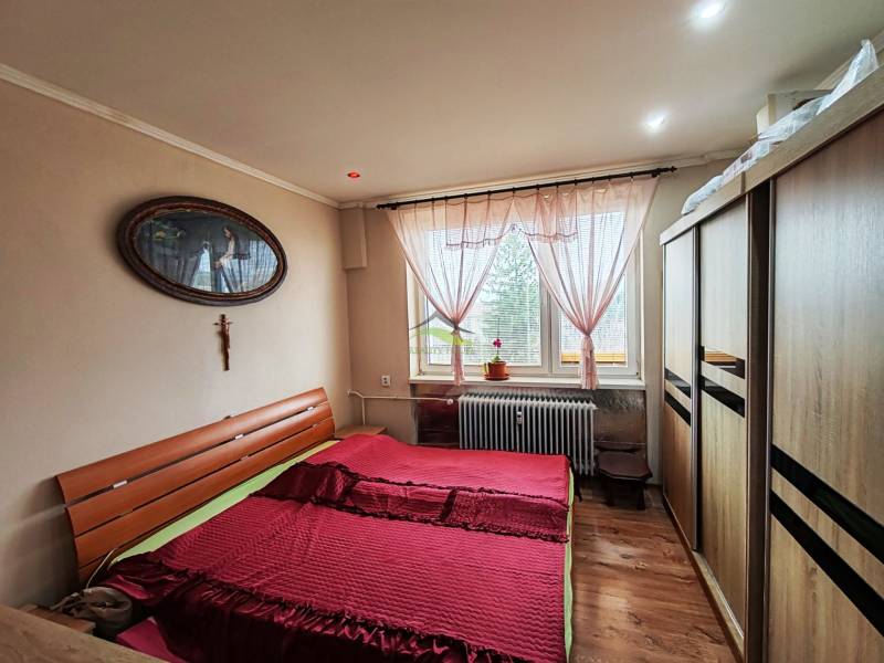 Ložnice ve 4pokojovém bytě s postelí, skříní a podlahou s dřevěným dekorem.