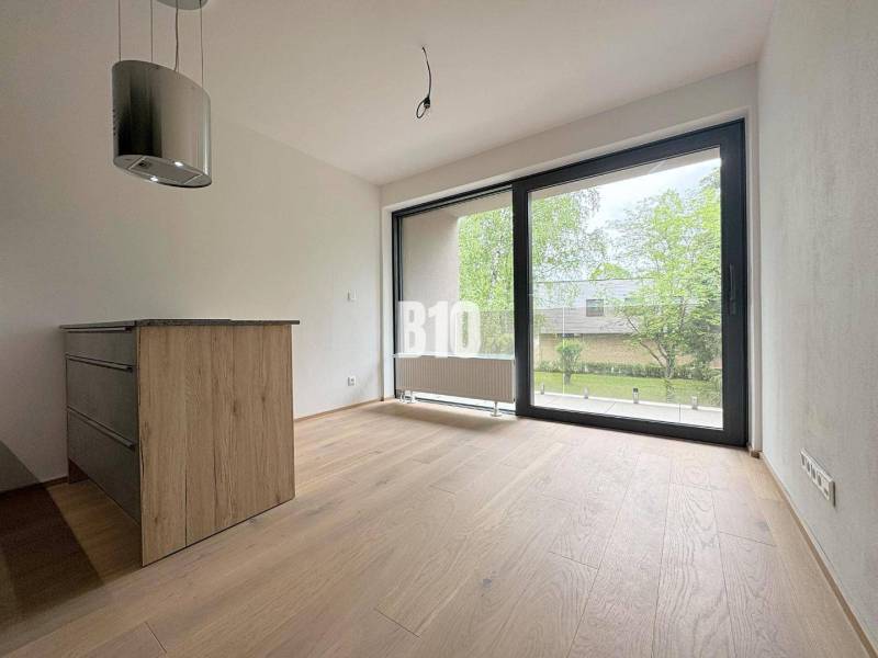 Interiér 2-pokojového bytu s dřevěnou podlahou a velkým oknem na zelený exteriér.