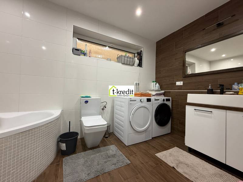 Koupelna v rodinném domě s vanou, pračkou, sušičkou a podlahou s dřevěným dekorem.
