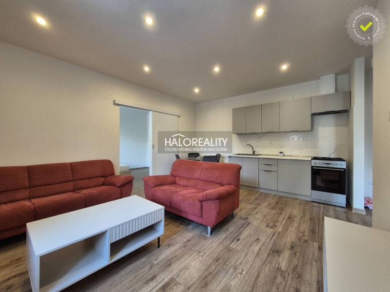 Obývací pokoj v 2-pokojovém bytě s podlahou s dřevěným dekorem, červené sedačky, kuchyně.