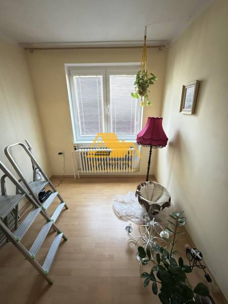 Pokoj s podlahou s dřevěným dekorem, rostlinou a růžovou lampou.