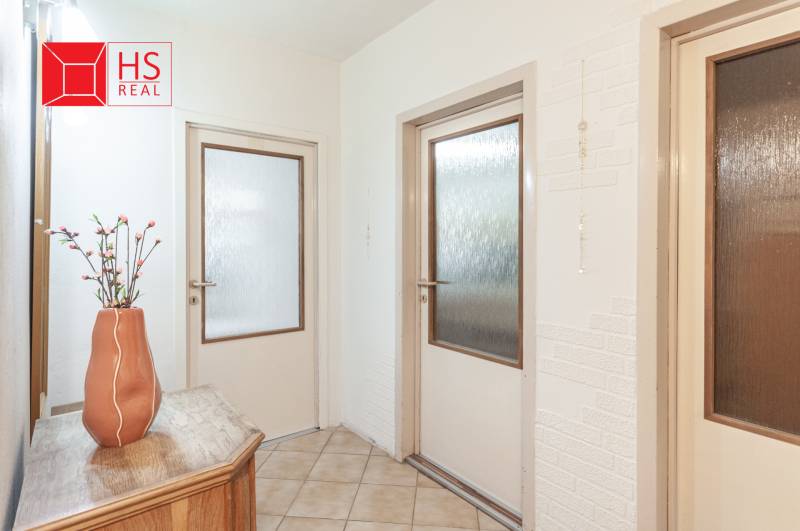 Chodba ve 3-pokojovém bytě s květinou na dřevěném stolku a dveřmi se sklem.