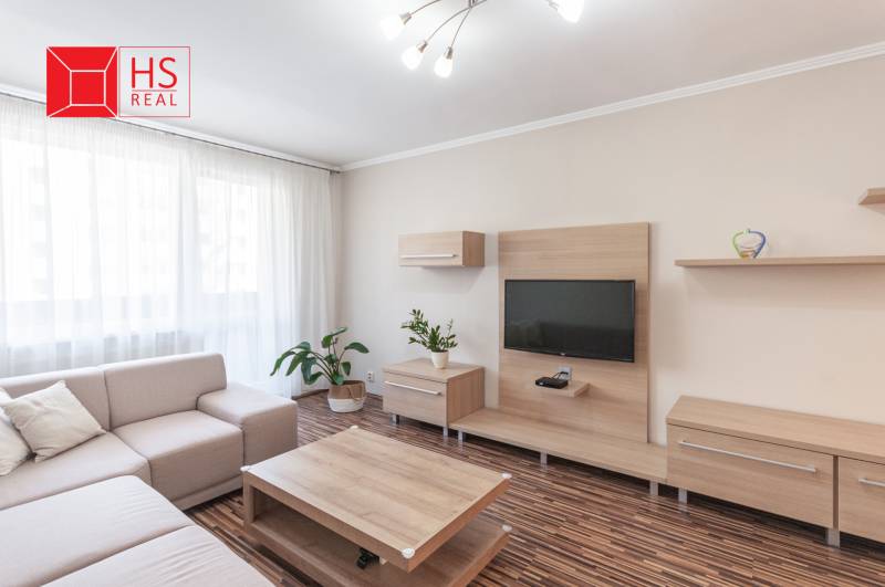 Obývací pokoj 3pokojového bytu s podlahou s dřevěným dekorem a pohodlnou sedačkou.