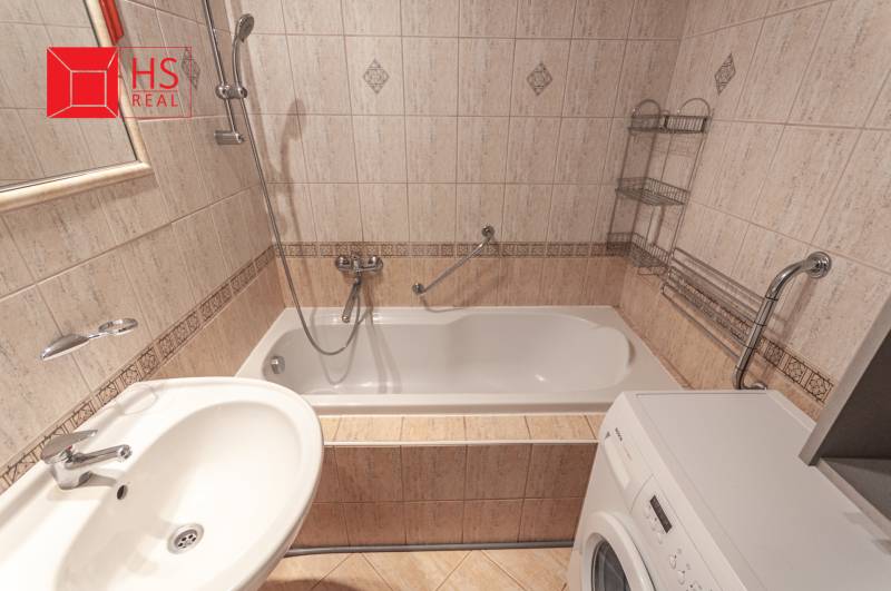 Koupelna v 3-pokojovém bytě s obklady, vanou a pračkou.