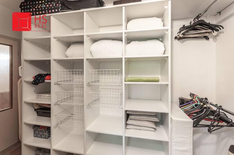 Úložný prostor s policemi a věšáky ve 3-pokojovém bytě s podlahou s dřevěným dekorem.