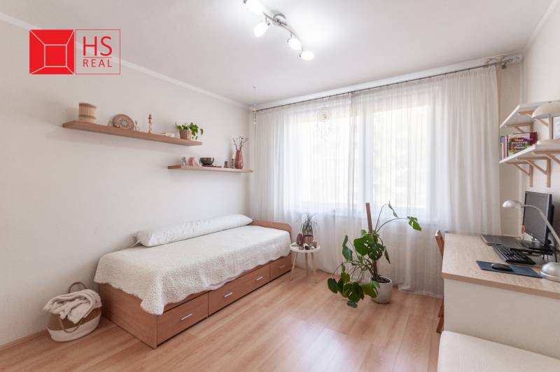 Světlý pokoj s postelí, psacím stolem a podlahou s dřevěným dekorem ve 3pokojovém bytě.