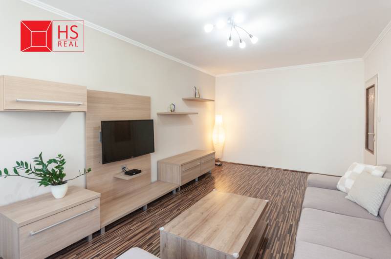 Obývací pokoj třípokojového bytu s podlahou s dřevěným dekorem a šedou pohovkou.