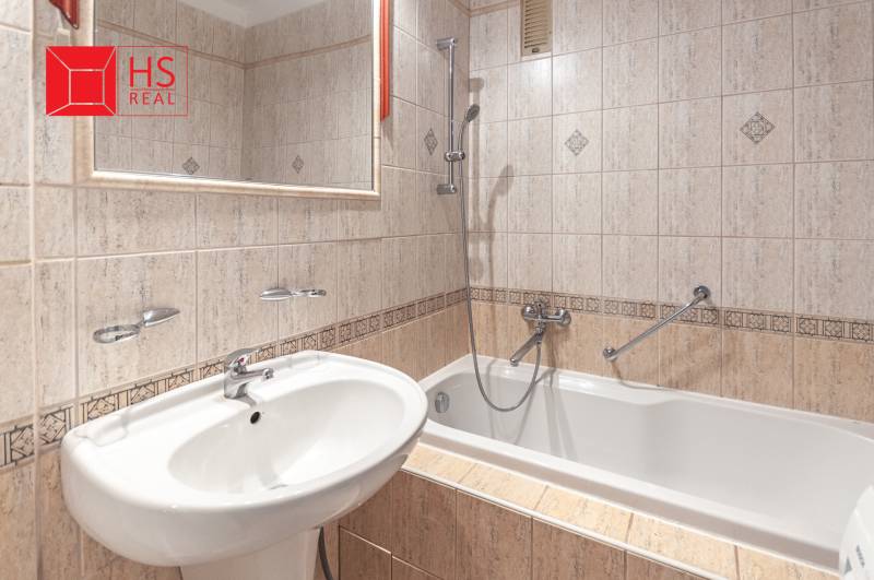 Koupelna v 3-pokojovém bytě s vanou, obklady a umyvadlem, doplněná zrcadlem.