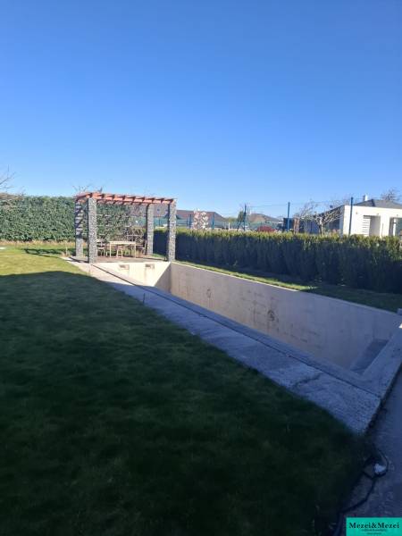 Zahrada rodinného domu ve Zvončíně s pergolou a nedokončeným bazénem.