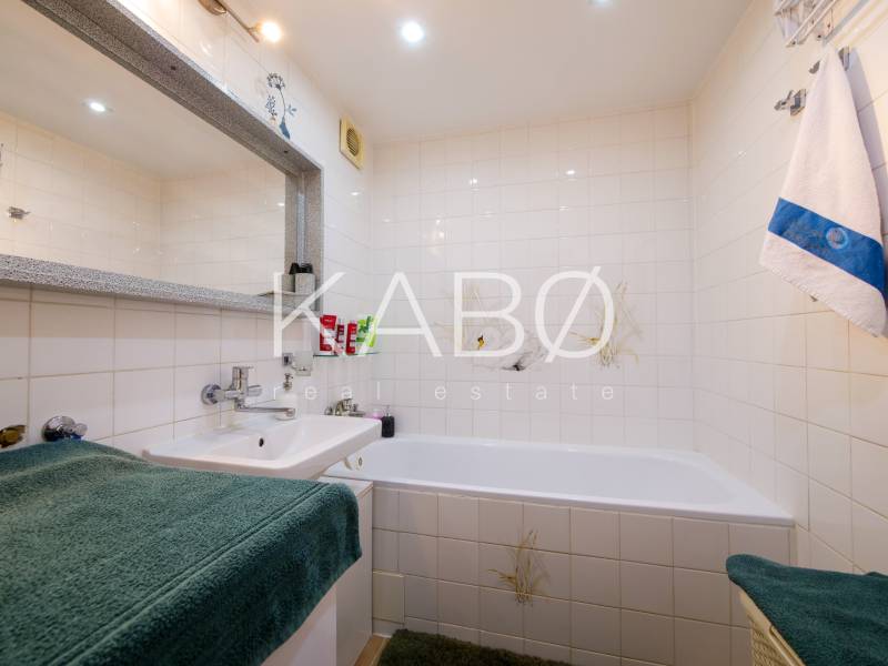 Koupelna ve 3-pokojovém bytě s vanou, umyvadlem a bílými dlaždicemi.