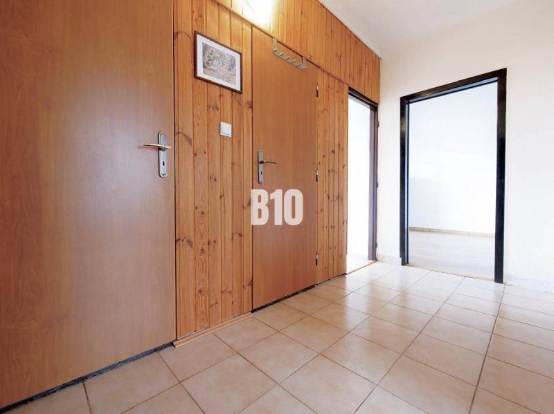 Chodba v 3-pokojovém bytě s dlažbou, dřevěným obložením a vstupy do dalších místností.