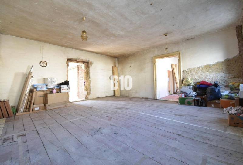 Nepořádná místnost v rodinném domě s dřevěnou podlahou a stavebním materiálem.