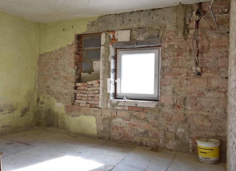 Pokoj v rodinném domě s cihlovými stěnami a kbelíkem na podlaze.