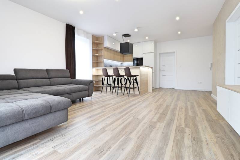 Obývací pokoj v 3-pokojovém bytě s pohovkou, barem a podlahou s dřevěným dekorem.