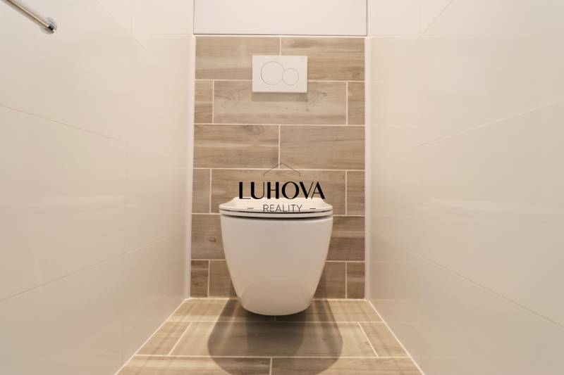 Toaleta s dřevěným dekorem a bílými obklady v 3-pokojovém bytě.