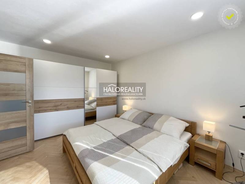 Ložnice s podlahou s dřevěným dekorem v 1-pokojovém bytě, světlá postel a šatník.