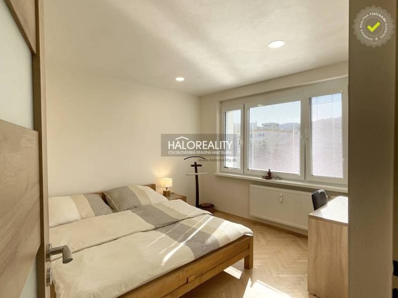 Ložnice v jednopokojovém bytě s podlahou s dřevěným dekorem a velkými okny.