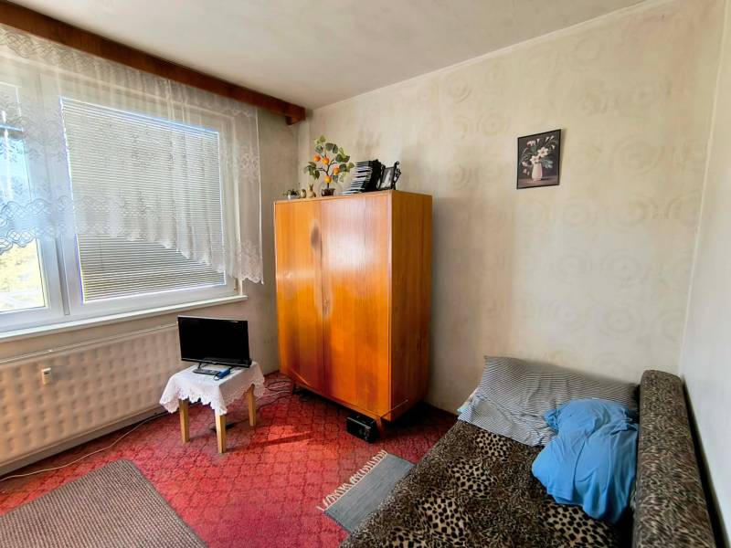 Pokoj v 3-pokojovém bytě se skříní, pohovkou a malou obrazovkou.