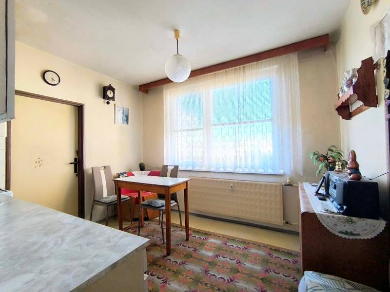 Jídelna s jednoduchým nábytkem v 3-pokojovém bytě, podlaha s dekorativním kobercem.