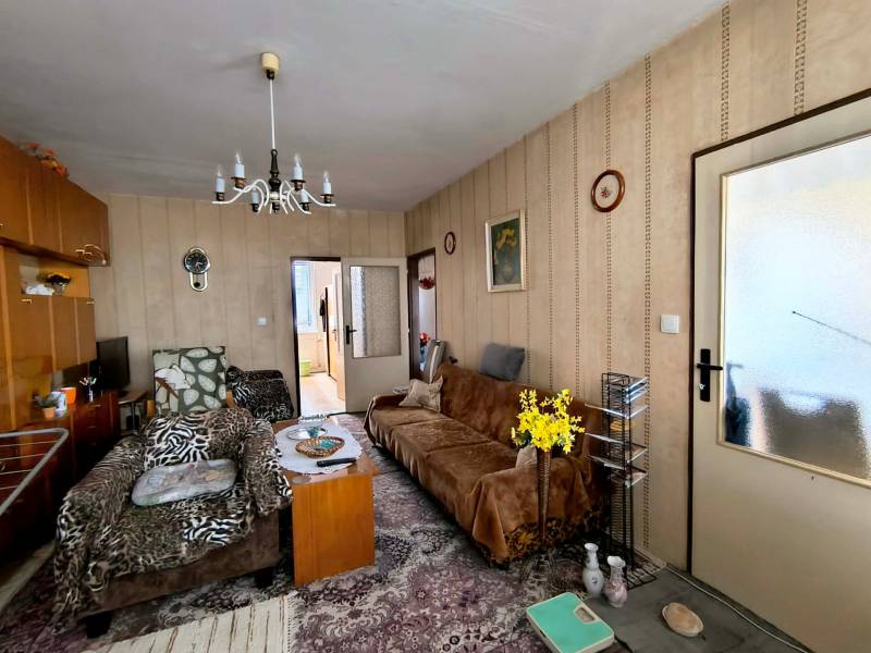 Obývací pokoj ve 3-pokojovém bytě s křesly, květinami a vintage lustrem.