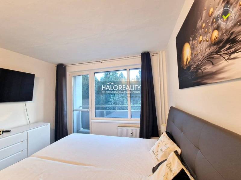 Ložnice v třípokojovém bytě s velkou postelí, televizí a balkonem.