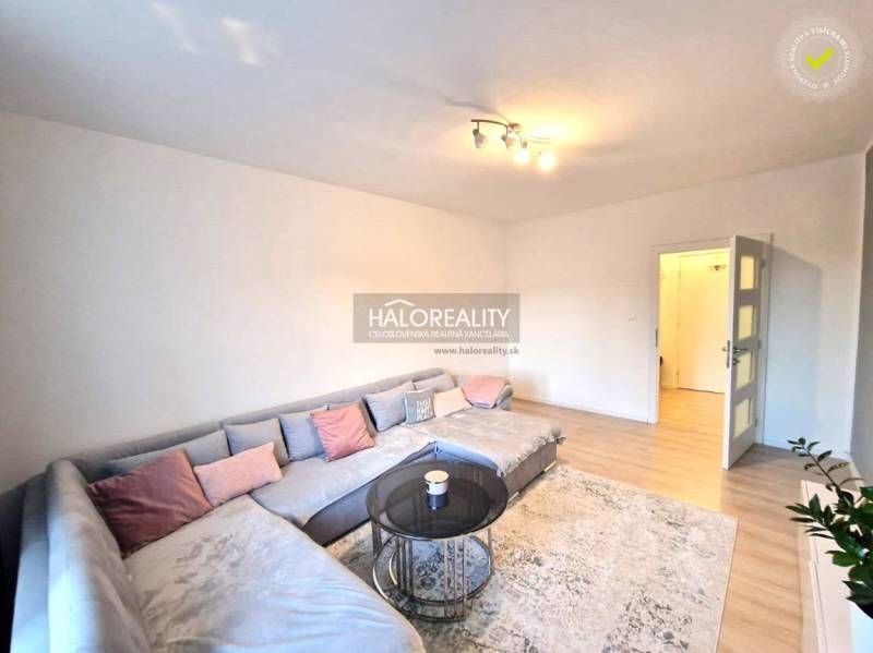 Obývací pokoj v 3-pokojovém bytě s velkou rohovou sedačkou a podlahou s dřevěným dekorem.